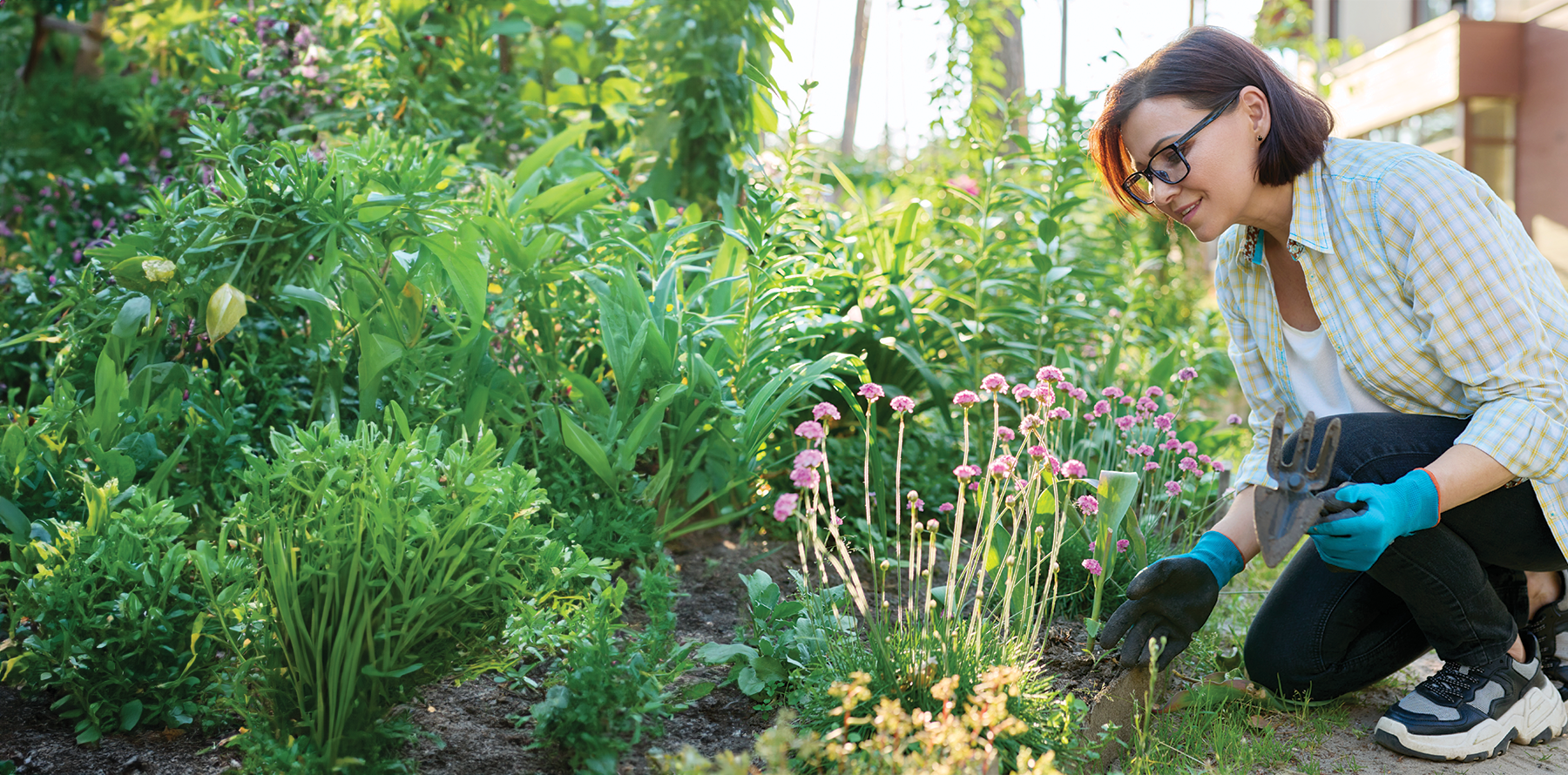 A lady enjoying her garden with gloves and a trowel.
